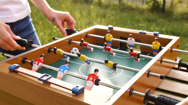Two person playing table foosball with red and yellow plastic players in a garden, capturing everyday joy and simple outdoor fun.