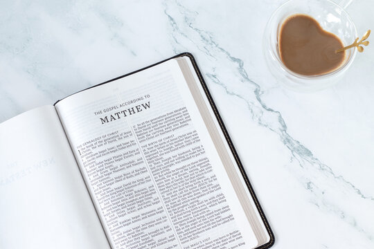 Matthew gospel in holy bible book with coffee cup on white marble background. Top view. Christian Scripture study concept.