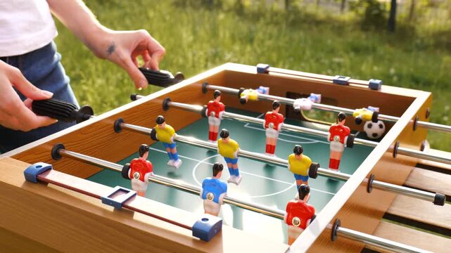 Two person playing table foosball with red and yellow plastic players in a garden, capturing everyday joy and simple outdoor fun.
