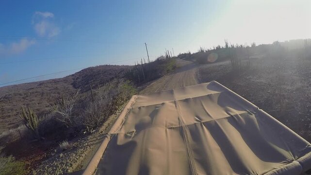POV shot of an off-road vehicle driving on a rugged dirt road in a desert landscape during golden hour