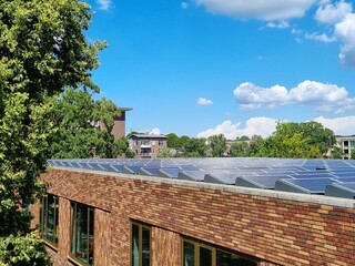 Horizontal view of modern Montessori school brick facade featuring a massive solar panel roof installation for renewable energy and corporate sustainability. © Shira GoralyHochberg