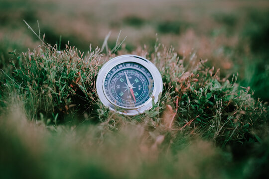 Compass on a rock in a grassy field representing navigation, guidance, exploration, and the journey toward the right direction.