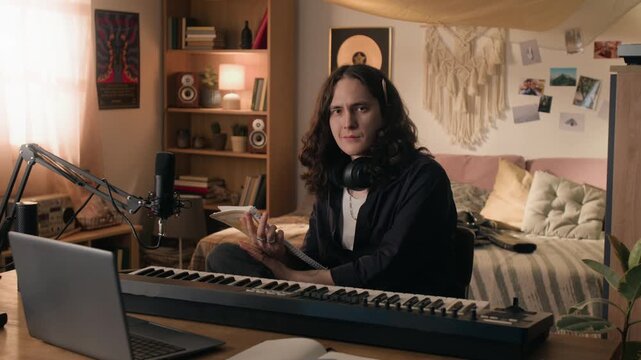 Portrait of young musician holding notebook and sitting at digital piano keyboard, looking at camera. Footage for online music education and e-learning advertisements