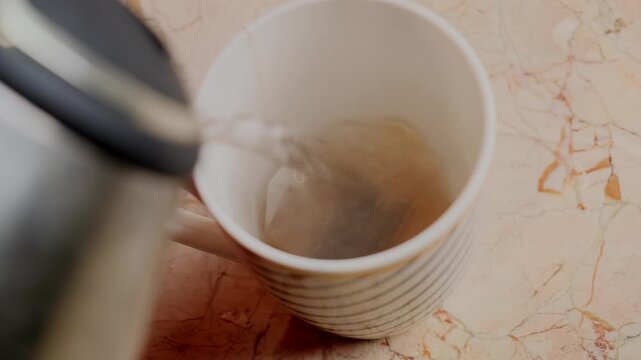 Brewing tea. White ceramic mug with tea bag steeping in hot water on marble surface. Simple minimalist tea preparation concept for food, lifestyle and beverage editorial content