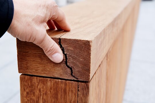 A close-up of a hand touching a cracked wooden beam, symbolizing damage, repair, and the need for renovation or restoration.