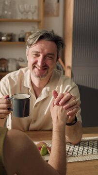 Vertical shot of middle aged Caucasian man holding hands with Caucasian woman and drinking coffee. Ideal for family lifestyle marketing, relationship counseling apps, or insurance commercials