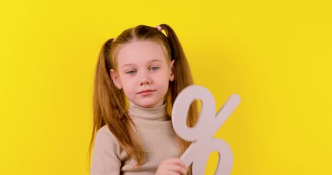 Video of a young blonde girl on a yellow background showing and removing a percentage symbol. Concept of discounts, sales, savings, shopping, finance, pricing, and special offers.