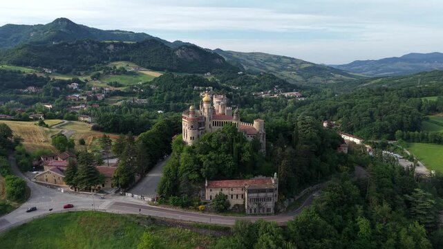 Drone aerial footage of Rocchetta Mattei rising above the Reno Valley. Historic castle with neo-medieval style, stone ramparts, and dramatic clouds in the Italian Apennines.