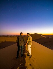 Fototapeta premium Two men standing on a sand dune at dusk