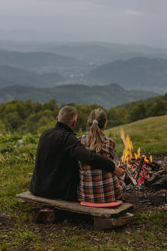 Couple sitting by a campfire overlooking misty mountain landscape at sunset. Romantic outdoor camping scene with scenic views, perfect for travel, adventure, hiking, nature and lifestyle concepts.