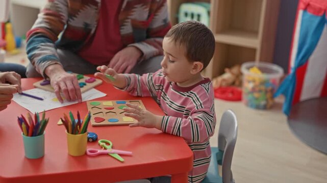 Man and little boy sort a wooden shape puzzle and exchange a high five, hands touching on a red table in a building; bonding joy.