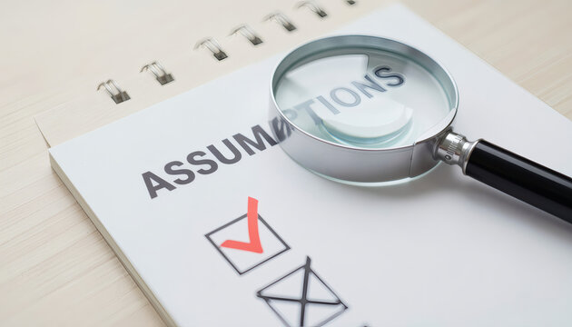 A Magnifying Glass Magnifying The Word Assumptions On A Notepad With A Checklist