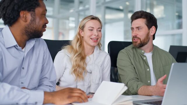 Happy multiracial business team three colleagues laughing emotional talking looking in laptop discussing online internet work task diversity workers laugh talk in office with computer funny arguing