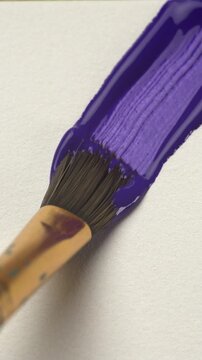 Artistic Creation Concept. Close-up paint brush applying acrylic violet color on white canvas. Texture and vibrant pigment