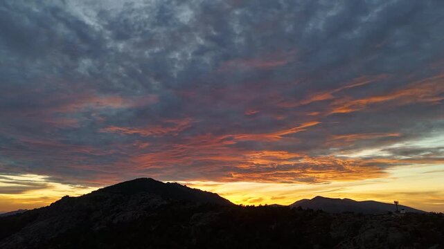 Hyperlapse aerial drone footage of a sunset with blue-gray clouds and pink streaks over the Sierra de Guadarrama mountains at Puerto de Navacerrada, Madrid, Spain
