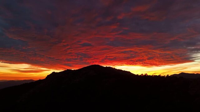 Hyperlapse aerial drone footage of a sunset over the Sierra de Guadarrama mountains at Puerto de Navacerrada, Madrid, Spain, with clouds moving over a silhouetted ridge