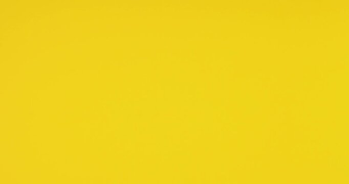 Close-up video of a female hand making a thumbs down gesture on a bright yellow background. Concept of dislike, rejection, negative feedback, disapproval, bad review, and criticism.