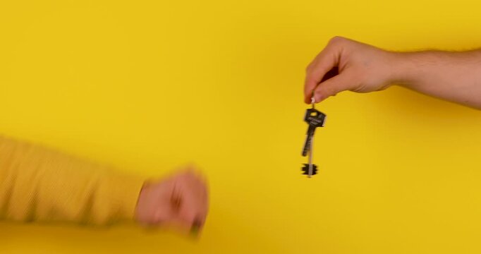 Close-up video of a female hand passing house or apartment keys on a yellow background. Real estate concept symbolizing home purchase, property rental, ownership transfer, and moving in.