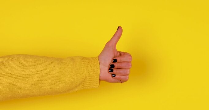 Close-up video of a female hand making a thumbs up gesture and moving it up and down on a bright yellow background. Concept of approval, positivity, success, recommendation, and positive feedback.