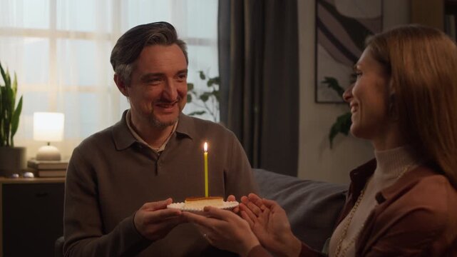 Medium shot of middle aged Caucasian woman presenting cake with lit candle to middle aged Caucasian man blowing it out. Footage ideal for family lifestyle commercials and relationship marketing