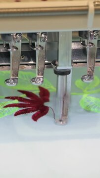 An advanced industrial embroidery machine swiftly brings a beautiful red leaf design to life on soft fabric.