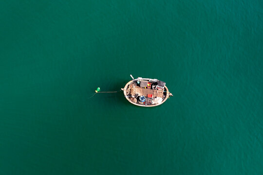 A traditional round Vietnamese basket boat, filled with fishing gear, floats peacefully on the rich emerald green sea during daylight