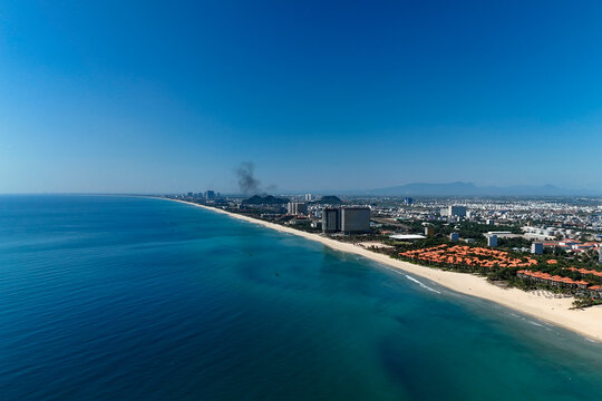 An aerial scene shows a long sandy beach curving along the coast of Da Nang City, Vietnam, with deep blue ocean water and a clear sky above