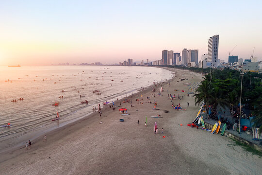Numerous people enjoy swimming, paddleboarding, and windsurfing on a long sandy beach in Da Nang, Vietnam