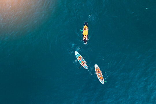Three pairs of people on stand-up paddleboards move gracefully over the deep blue ocean