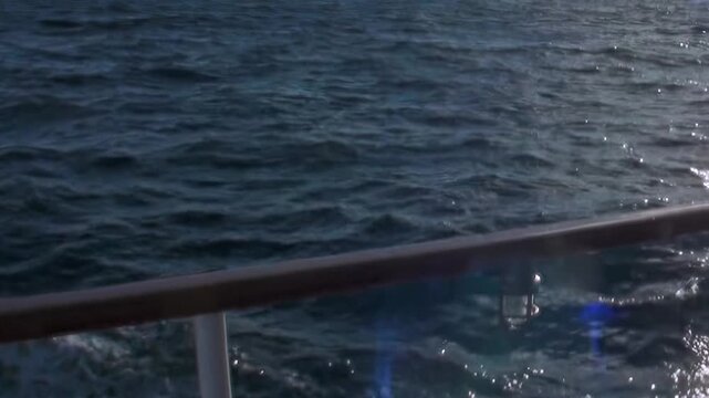 A vessel journeys across the immense Arctic Ocean under the sun's gleam. Gaze at the deck railing as restless waves churn, reflecting blue hues from below, an extreme polar expedition.