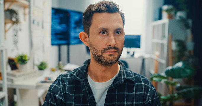 Young Caucasian male programmer writes code using multiple screens in home office workspace. AI development, cybersecurity, network database system, software engineering, remote tech startup concept.