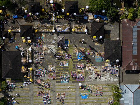 Aerial view of people gathered for Kuningan Day celebrations in a traditional temple courtyard with offerings and ceremonial umbrellas in Kecamatan Kintamani, Bali, Indonesia.