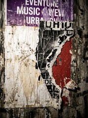 Fototapeta premium Gritty urban wall texture featuring layers of torn vintage concert posters and weathered paper scraps in a dark moody street alleyway