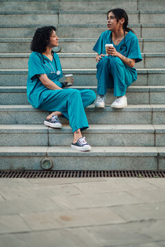 Healthcare workers relaxing on stairs with coffee, discussing work during a short break outdoors