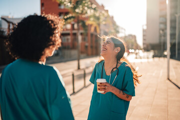 Happy medical professionals smiling and laughing during a coffee break, enjoying conversation on a city street at sunset