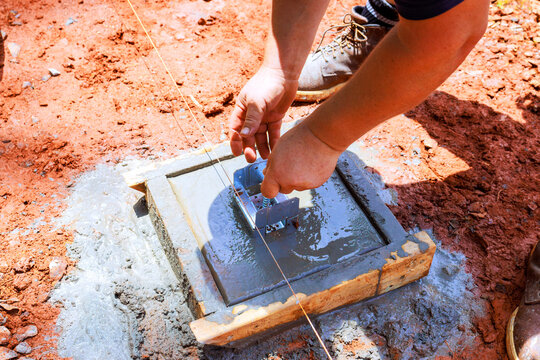 Contractor is install anchor bracket placing concrete in wooden frame on construction site