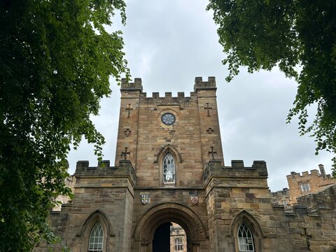 Historic Stone Tower Approach: A striking rectangular castle tower adorned with sacred crosses and classic defense cuts peaks out dynamically from behind a rich green forest canopy.