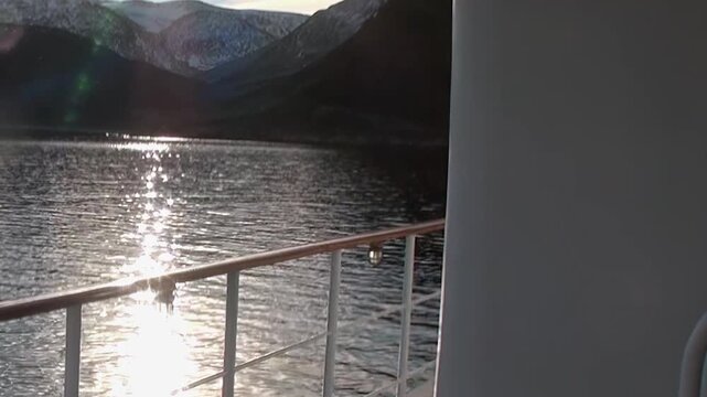 Captivating view aboard ship sailing Arctic Ocean. Golden sunlight shimmers brightly across calm water, creating dazzling path. Distant mountains frame this tranquil morning or evening vista.
