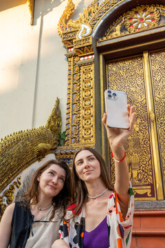 Two Friends Take a Selfie Near a Gold Decorated Wall in Thailand