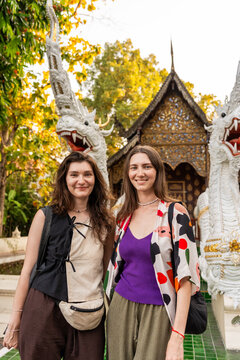Two Women Stand in Front of Temple With Dragon Statues in Thailand
