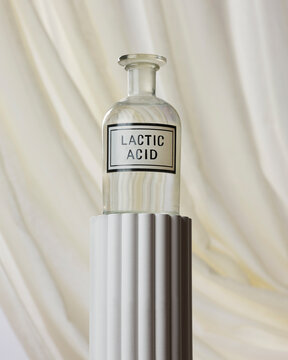 A bottle with 'lactic acid' written on it on a column against white