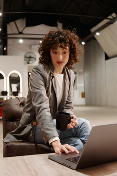 Woman Works on Laptop While Holding a Cup in a Modern Space