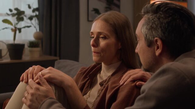 Close up of middle-aged Caucasian man comforting pensive middle-aged Caucasian woman on sofa, gently caressing wife. For mental health awareness, relationship counseling, or family support campaigns