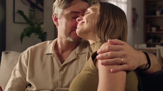Close up of middle aged Caucasian man and adult Caucasian woman embracing on sofa with closed eyes, sitting closely. Clip ideal for relationship counseling or family lifestyle marketing