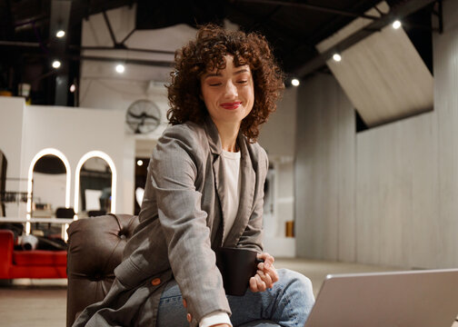Woman Sitting With Coffee and Working on Laptop in a Modern Space