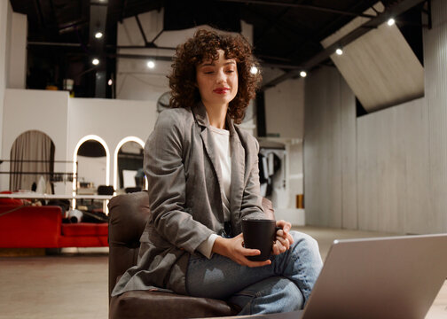 Woman Sitting With Coffee While Working on Laptop in a Modern Space