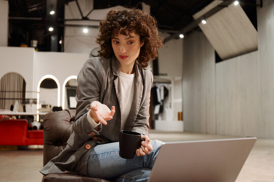 Woman Sits in a Caf&eacute; Holding a Cup While Using a Laptop