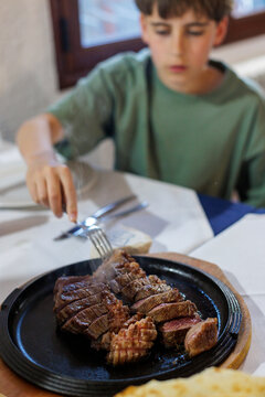 A teenager picks a part of a steak