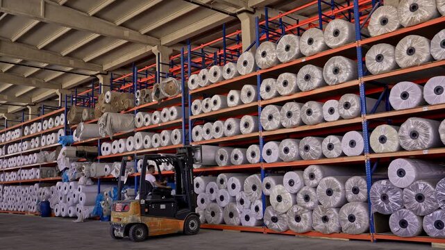 Yarn bobbins are stored on high shelves inside a textile warehouse with forklift operation. This video frame shows stock management, raw material storage, logistics, and industrial warehouse layout.