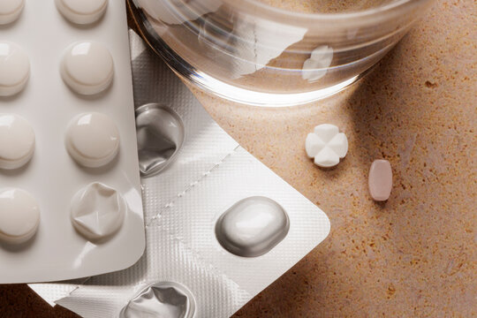 Pill strips with two separate pills next to a glass of water